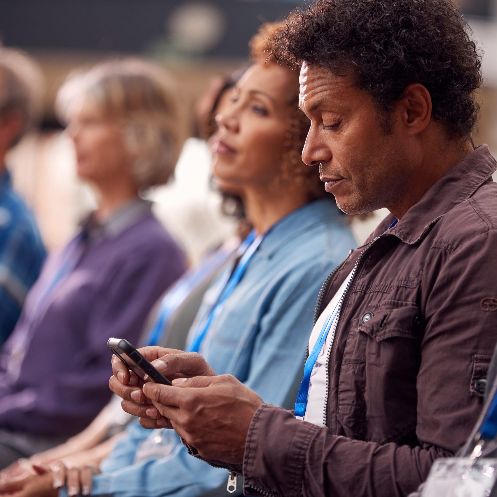 Businessman In Presentation At Conference Checking Mobile Phone